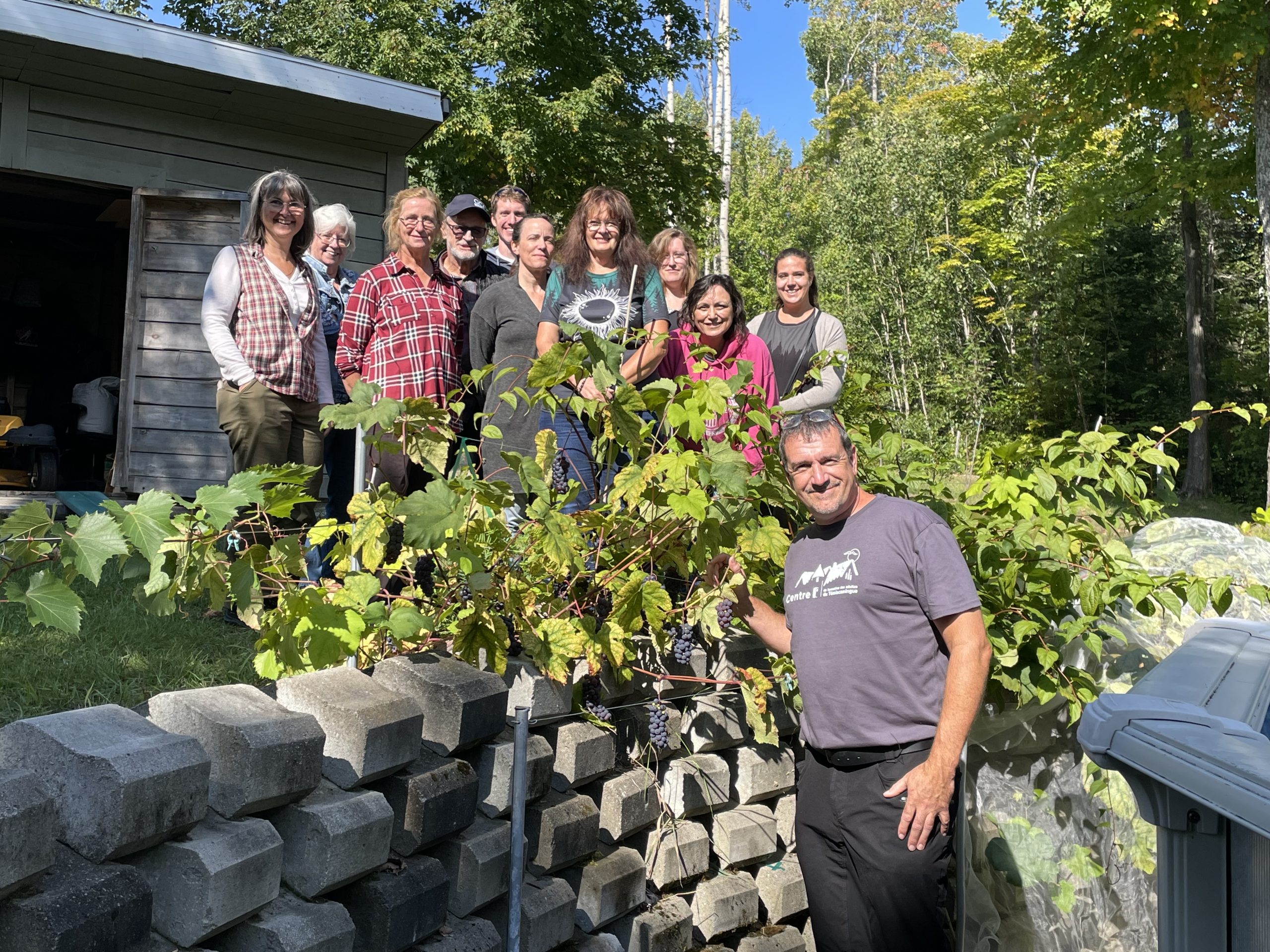Michel Tessier prend la pose devant des vignes et devant une classe à qui il a enseigné son savoir sur la culture d'arbres fruitiers.
